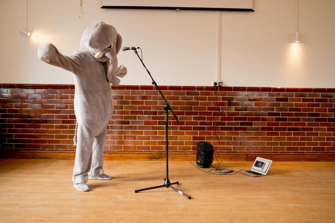 A person dressed as an elephant speaks into a microphone