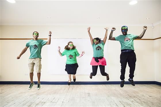 Four people wearing green t-shirts and superhero masks jumping in the air