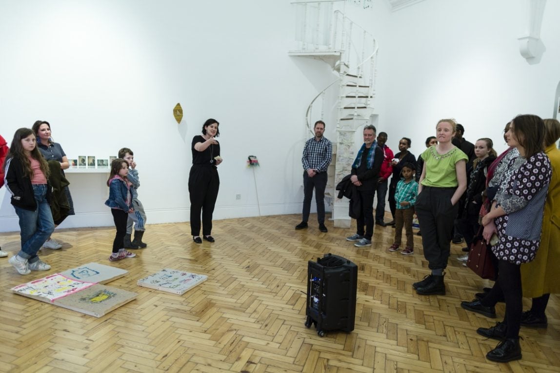a group of people in an art gallery looking at an exhibiton, there is a speaker in the middle of the floor