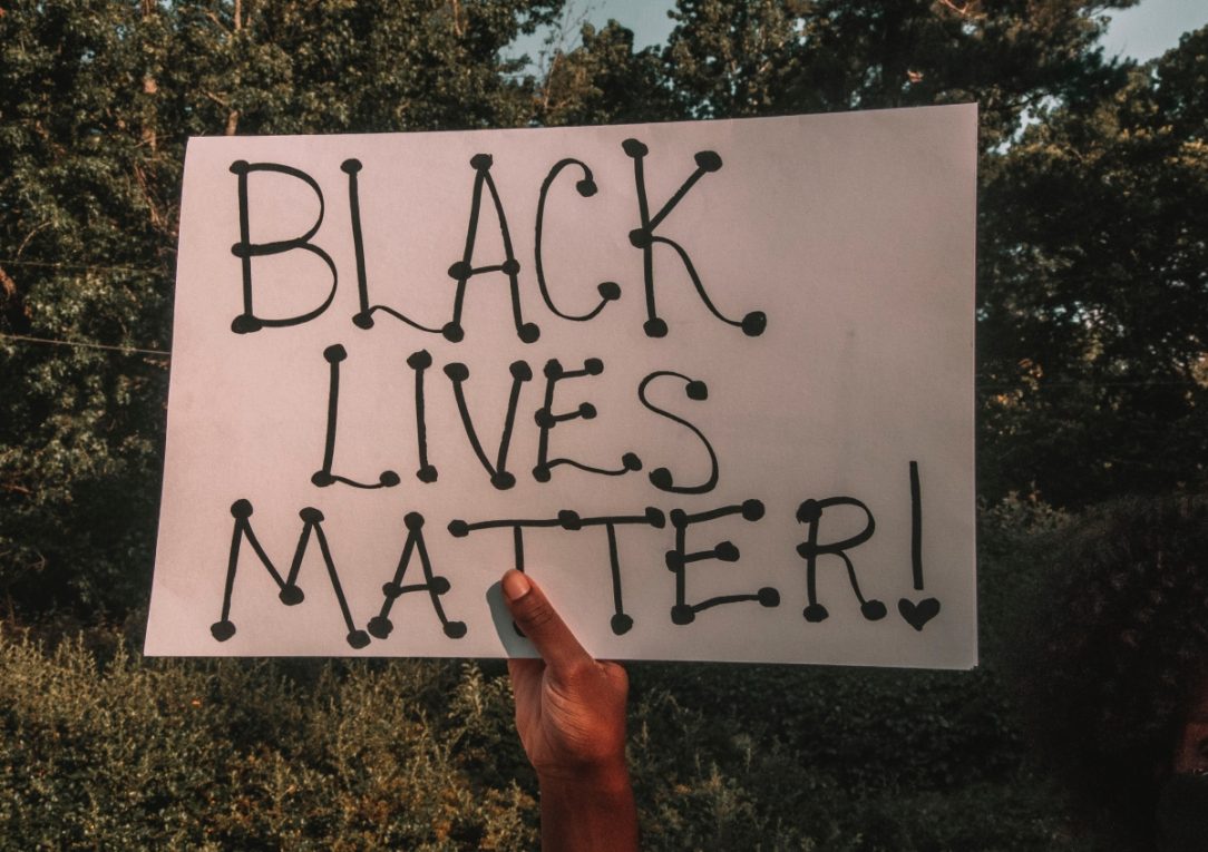 A hand holding a sign which reads 'Black Lives Matter'