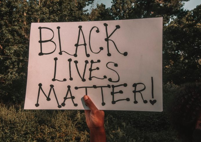 A hand holding up a sign that reads 'Black Lives Matter'