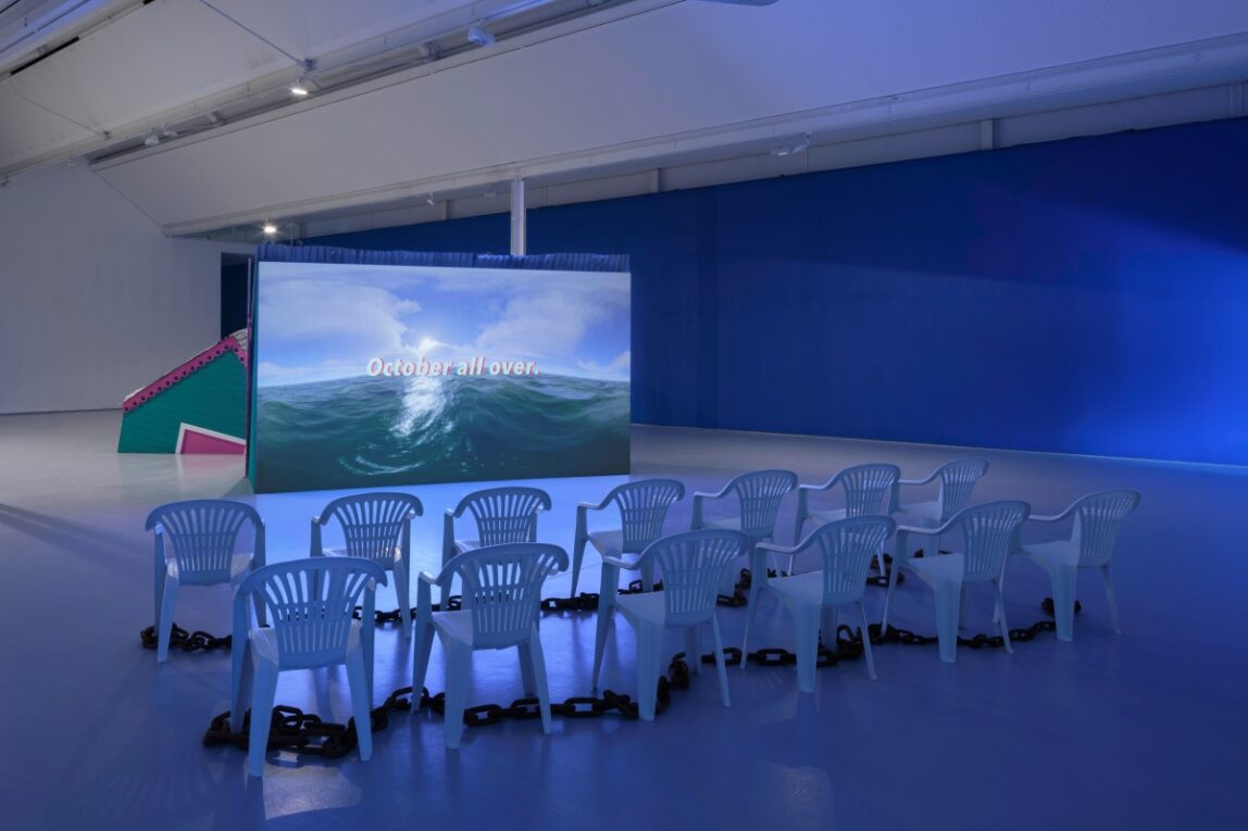 A screen which is projecting an image of the sea with the words 'October all over', there are two rows of empty chairs