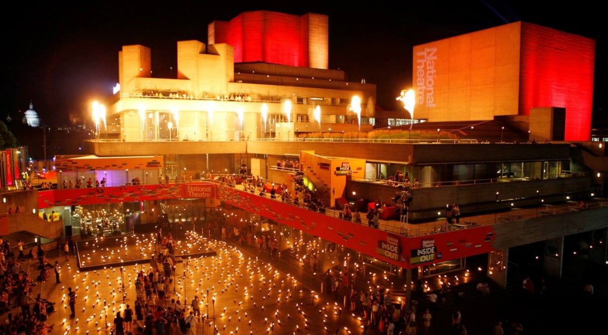 Outside of the National Theatre at night, a brutalist building in London, lit up by spot lights