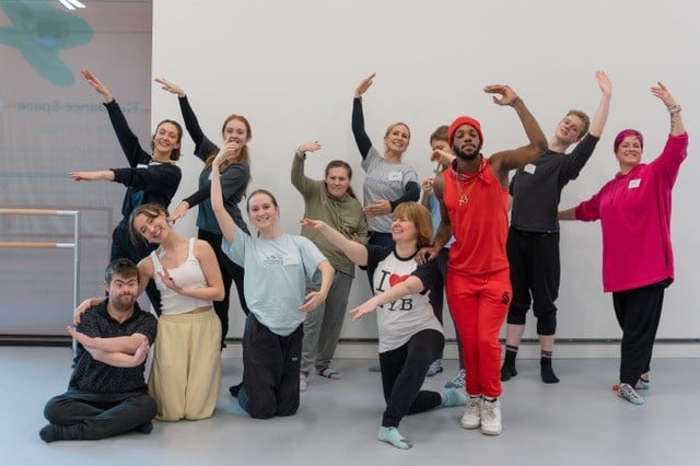A group of dancers in a studio posing for the camera in ballet positions