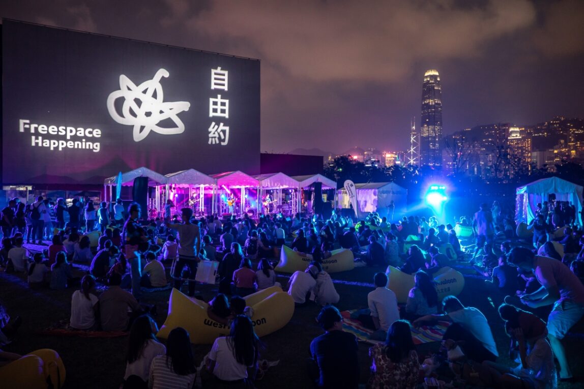 An outdoor film screening at night, the crown sits on blankets and beanbags