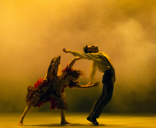 Two dancers in a dramatic pose against a yellow, smoky background
