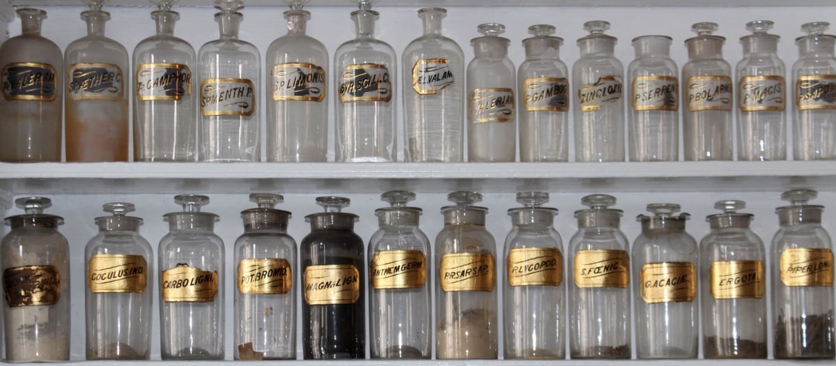Rows of old fashioned medicine bottles on a shelf with gold labels.