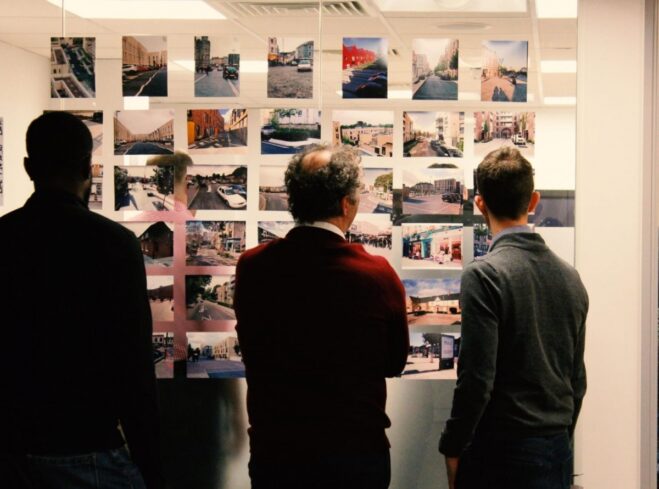 Three people looking a wall which is displaying photographs