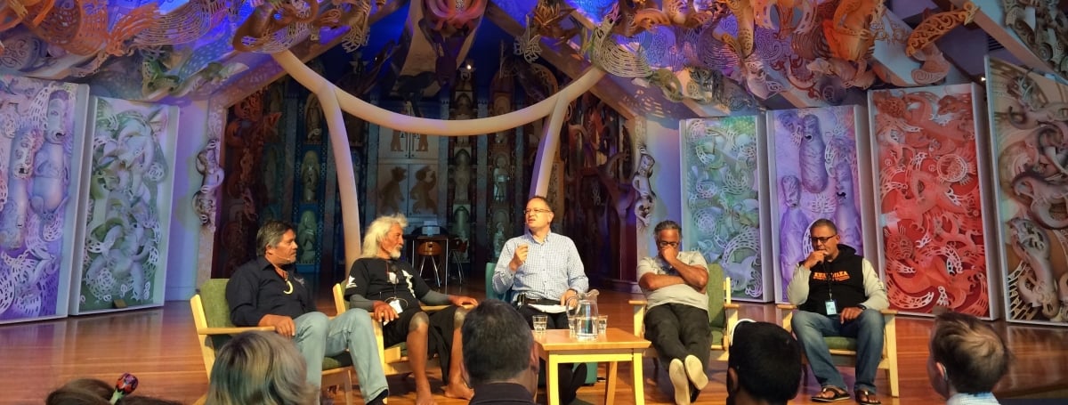 Five men on a stage, taking part in a panel discussion in front of an audience. 