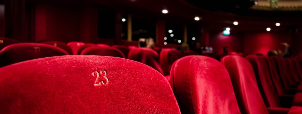 Photo by Kilyan Sockalingum on Unsplash Red velvet theatre style row seating under dim house lights.