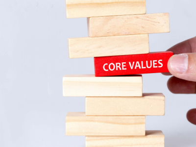 a stack of jenga blocks, a hand pulls out a block in the middle which has 'core values' written on it