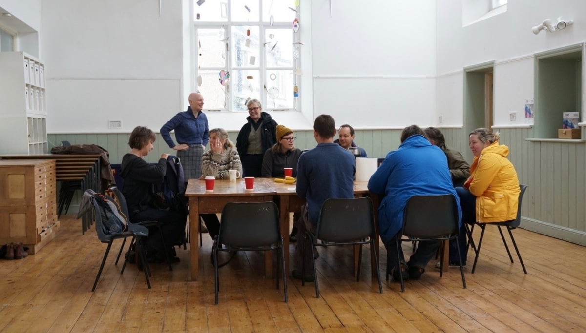 A group of people sat around a table drinking hot drinks and having a discussion