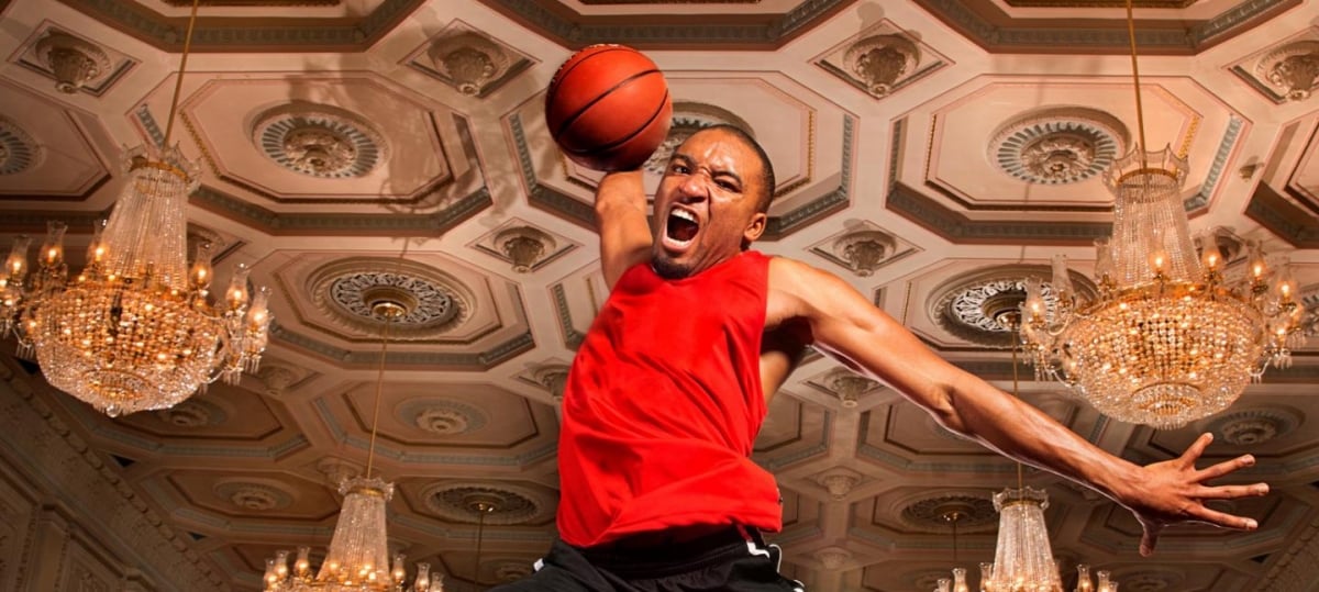 A basketball player is jumping with a basketball in a room with chandeliers