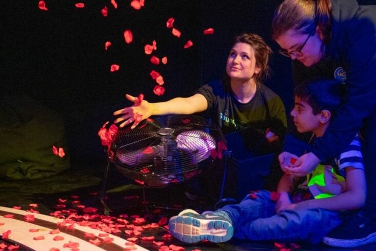 Ellie Griffiths sat on the floor throwing red petals into the air. A child sits on the floor watching