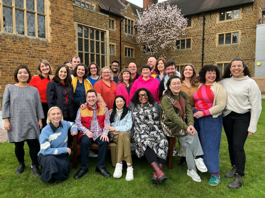 Group of Clore19 Fellows standing and sitting on a bench outside the exterior of Ashorne Hill Conference Centre