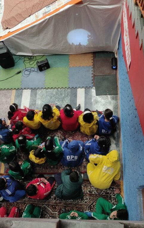 Group of people in brightly coloured t-shirts sitting before a makeshift stage in India