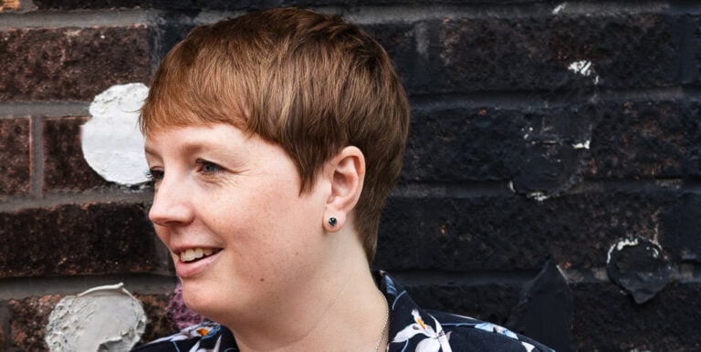 Headshot of Rachel Moorhouse, they have short brown hair and are wearing a black floral shirt