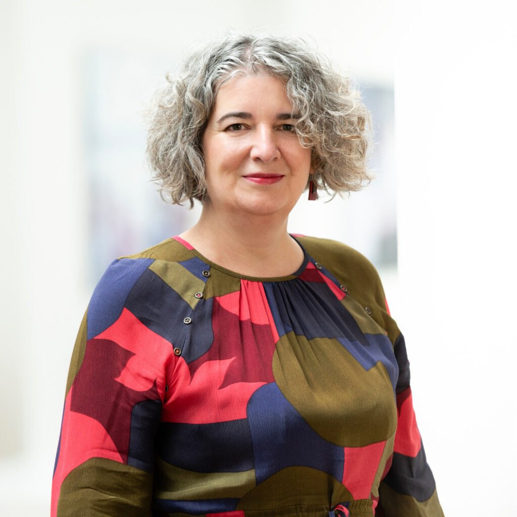 Headshot of Moira Sinclair, she is wearing a multicoloured shirt and smiling 