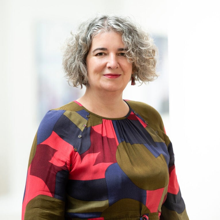 Headshot of Moira Sinclair, she is wearing a multicoloured shirt and smiling