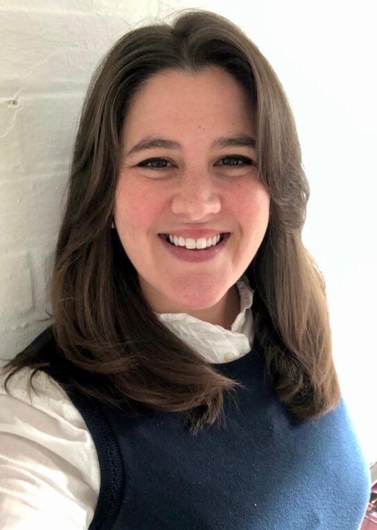 Katherine Osborn has shoulder length brown hair and is wearing a white long-sleeve shirt and navy sweater vest. 