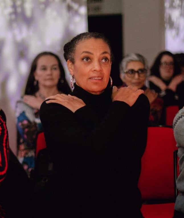 A photo of Rose Kigwana, she is wearing a black turtle neck and has her arms crossed across her chest