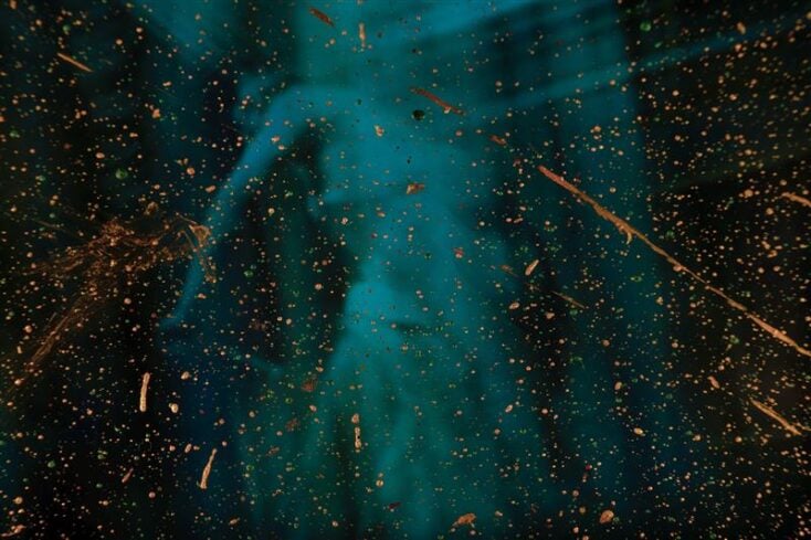 An abstract image of dark turquoise paint splattered with gold accents